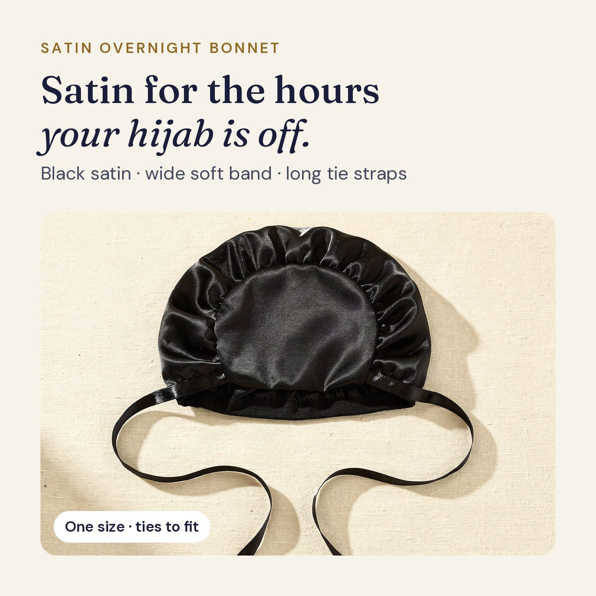 Black satin overnight bonnet with a wide soft band and long tie straps, laid flat on ivory linen